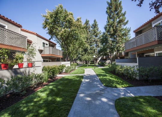 a walkway between two apartment buildings with grass and trees at Valley Plaza Villages, Pleasanton, 94566