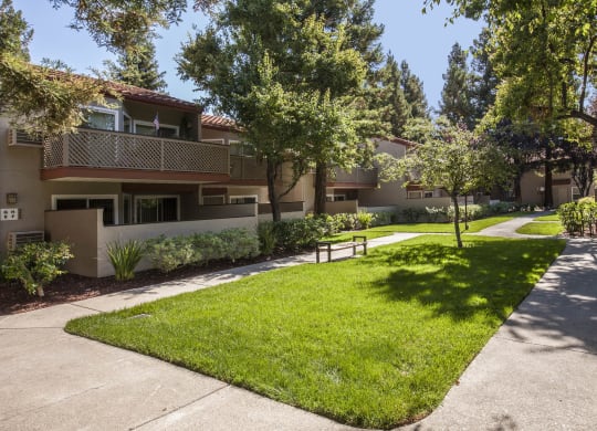 a sidewalk in front of an apartment building with grass and trees at Valley Plaza Villages, Pleasanton, California