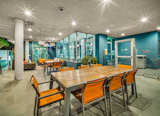 A long wooden table is surrounded by orange chairs in a room with a glass wall. at Esprit Apartments, California