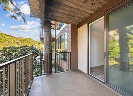 A balcony with a glass door and a view of trees.