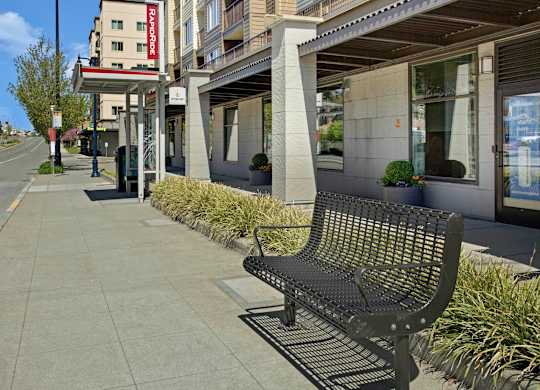 A black bench is on a sidewalk in front of a building.