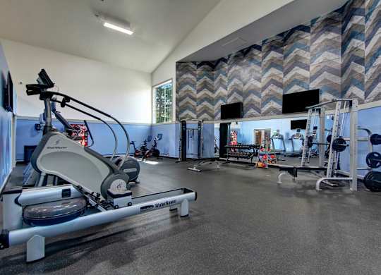 A gym with a rowing machine and a wall of mirrors.