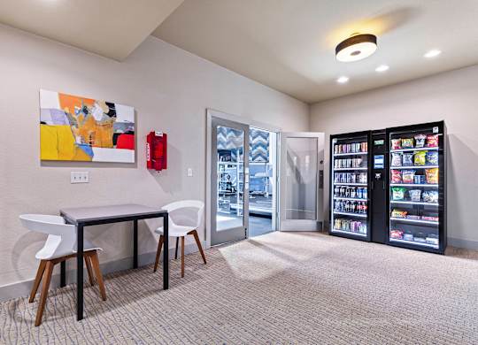 A room with a table, chairs, a fridge, and a painting on the wall.