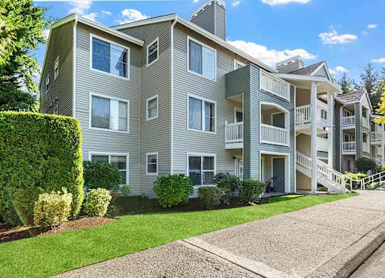 Gray apartment building with balconies, walkways, and lush green landscaping.