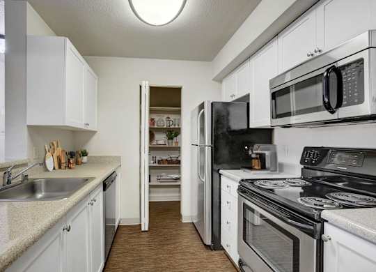 Galley kitchen with white cabinetry, dark appliances, and generous counter space.
