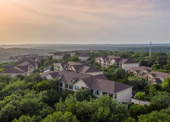 a neighborhood of houses surrounded by trees with a sunset in the background at The Verandah, Austin, 78726