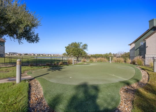a putting green with a house and trees in the background at The Fairways at Star Ranch, Hutto, Texas