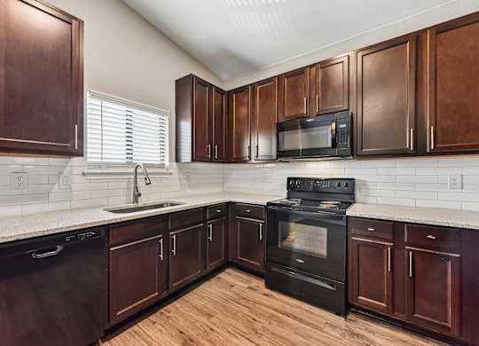 A kitchen with dark wood cabinets and black appliances.