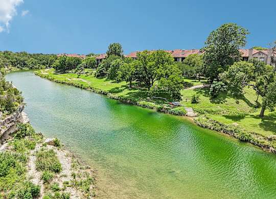 A river flows through a lush green landscape with a building in the background.