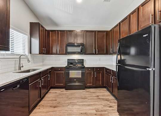 A kitchen with dark wood cabinets and a black refrigerator.