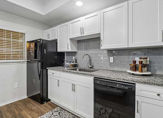 A kitchen with white cabinets and a black refrigerator.