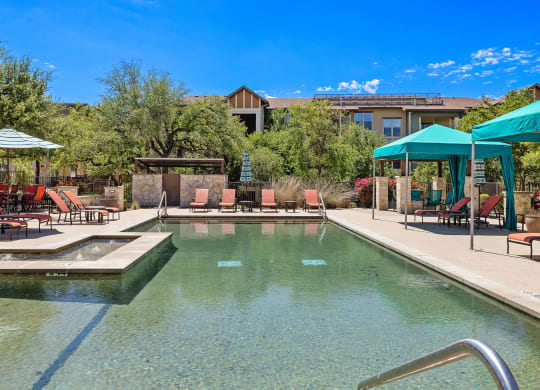 a swimming pool with chairs and umbrellas and a building in the background at Lakeline East Apartments, Texas, 78613
