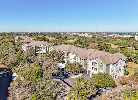 A large, multi-story residential building surrounded by trees at Legends on the Green Apartments, San Antonio, TX