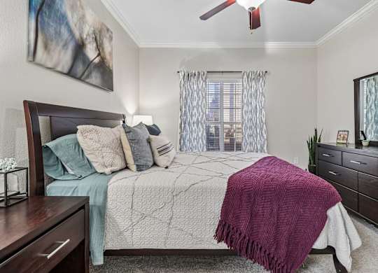A bedroom with a bed, a ceiling fan, and a painting on the wall.