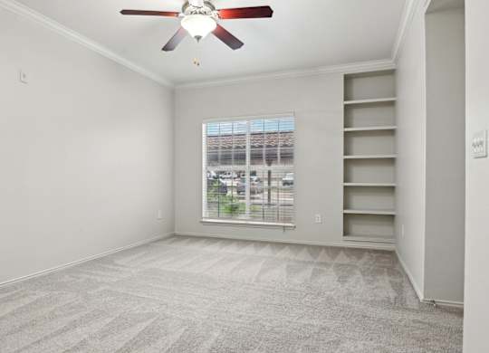 A room with a ceiling fan and a window overlooking a parking lot.