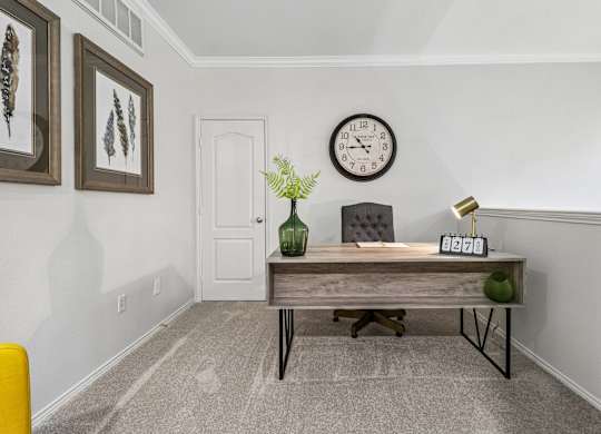 A room with a white door, a clock on the wall, and a table with a vase and a plant on it.