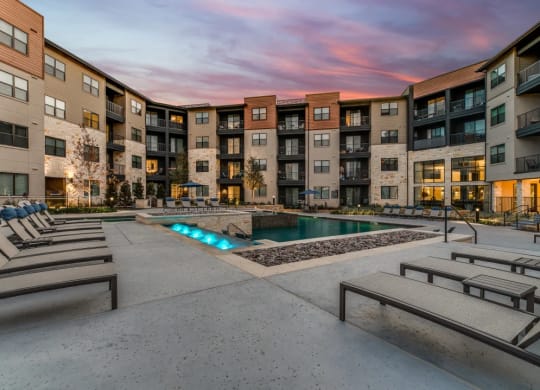 a swimming pool with chaise lounge chairs in front of an apartment building  at Aurora Watson Branch, Texas, 76063