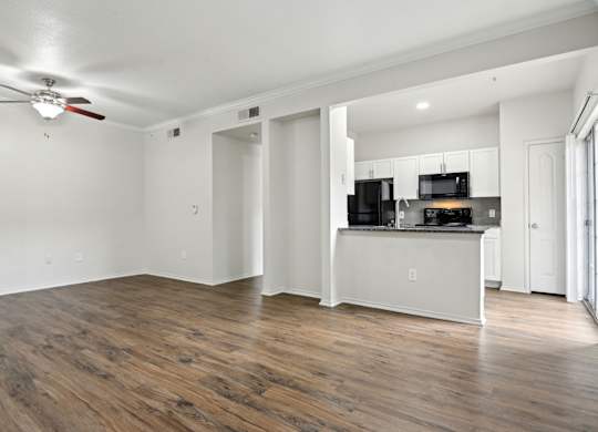A room with a ceiling fan and a kitchen area with a microwave, oven, and refrigerator.