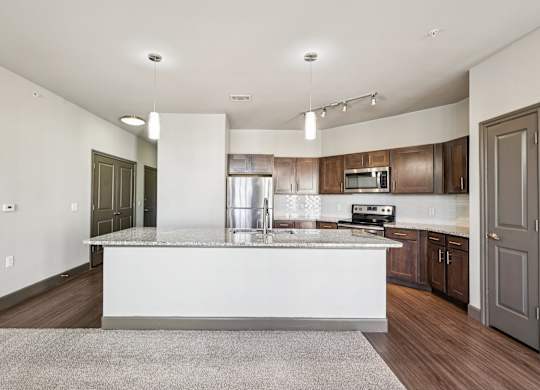 A modern kitchen with a white island and wooden cabinets.at North Creek, Hutto, 78634