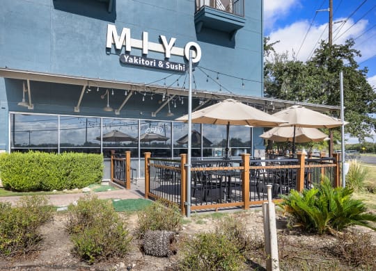an outdoor patio with umbrellas and tables in front of a blue building at Artisan Apartments & Shops, Texas