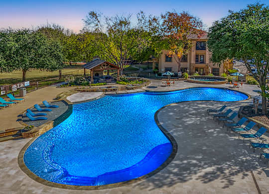 A large blue pool surrounded by trees and a building  at The Canyons Apartments, Texas, 76116
