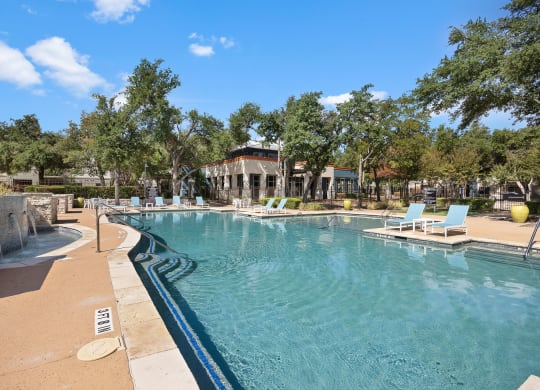 a resort style pool with lounge chairs and trees in the background at Artisan Apartments & Shops, Austin, TX