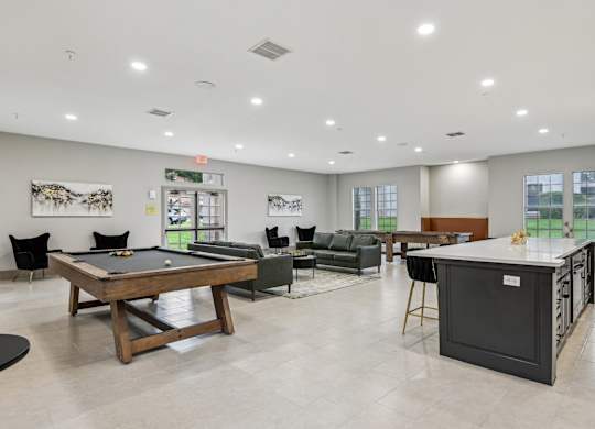 A billiard table is in the middle of a room with a pool table, a couch, and a bar.