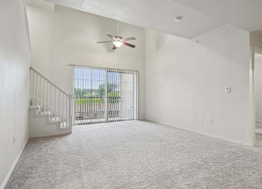 A room with a ceiling fan and a window with a view of a fence and trees.