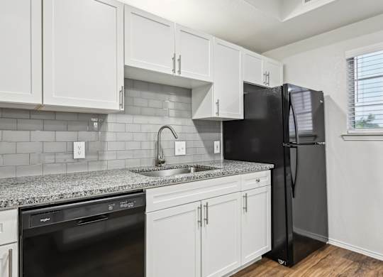 A kitchen with white cabinets and a black refrigerator.