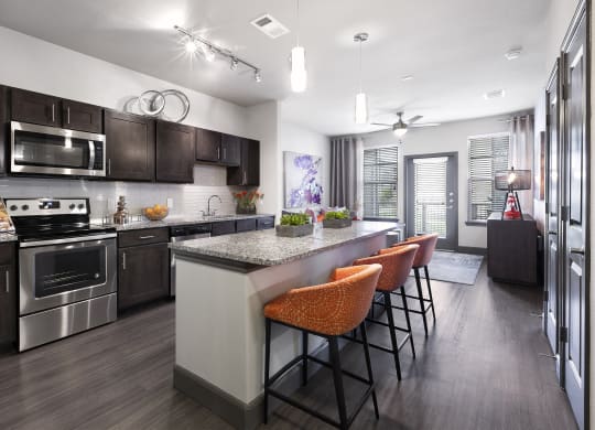 a kitchen with stainless steel appliances and a large island with chairs at North Creek, Texas, 78634