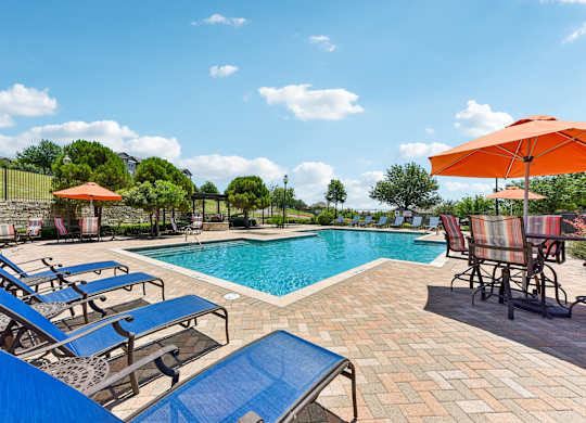 A pool with blue loungers and chairs and an orange umbrella.