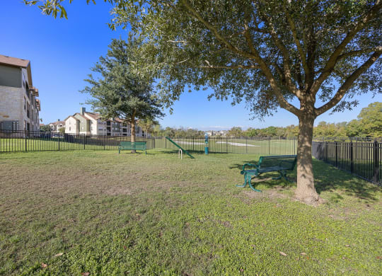a park with a tree and a tennis court in front of a building at The Fairways at Star Ranch, Hutto, Texas