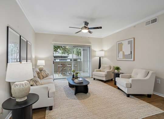 A living room with a white couch, two chairs, a coffee table, and a ceiling fan.