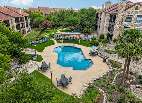 A swimming pool surrounded by lawn chairs and trees.