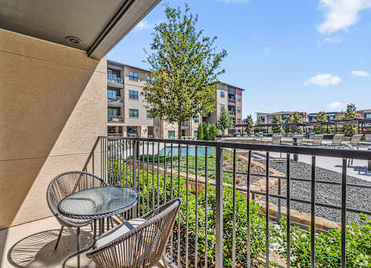 A balcony with a chair and table overlooking a pool and buildings.