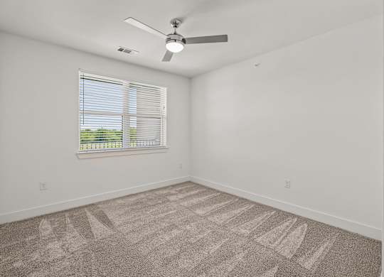 A room with a fan, carpet, and a window.
