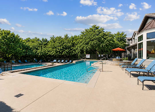 A large outdoor swimming pool surrounded by trees and lounge chairs.