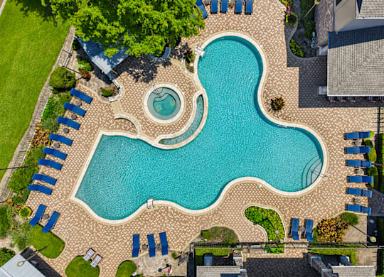 A large blue swimming pool surrounded by a brick patio and lounge chairs.