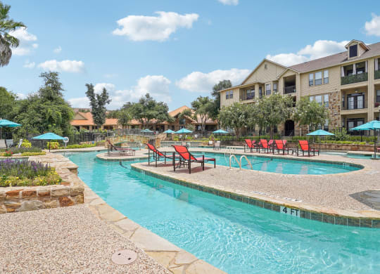 a swimming pool with chairs and umbrellas in front of an apartment building at The Verandah, Austin, TX