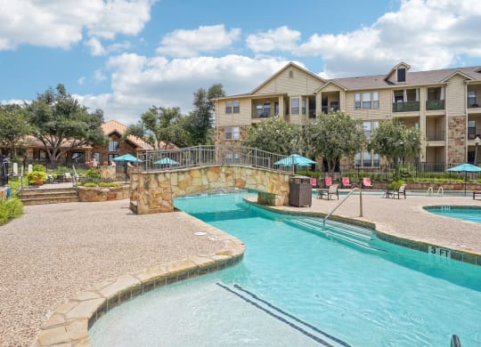 a swimming pool with a stone bridge over it next to an apartment building at The Verandah, Austin, TX, 78726