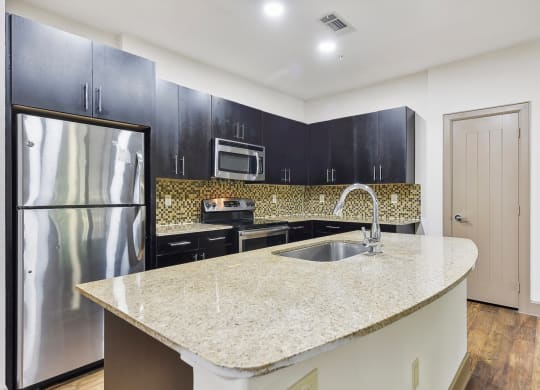 a kitchen with black cabinets and a granite counter top and a stainless steel refrigerator at Lakeline East Apartments, Cedar Park