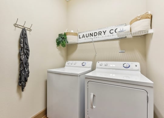 a washer and dryer in a laundry room with a shelf on the wall at Lakeline East Apartments, Cedar Park, TX
