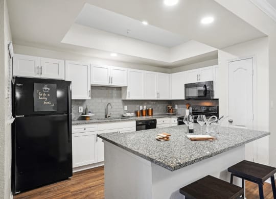a kitchen with a granite counter top and a black refrigerator at La Ventura Apartments, Plano, Texas