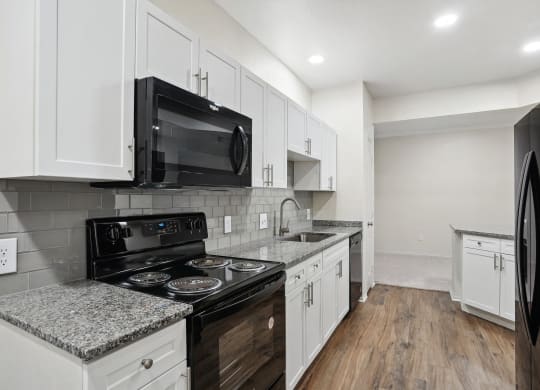 a kitchen with white cabinets and black appliances and a black microwave at La Ventura Apartments, Plano, 75093