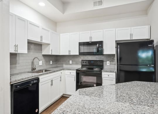 a kitchen with granite counter tops and black appliances at La Ventura Apartments, Texas, 75093