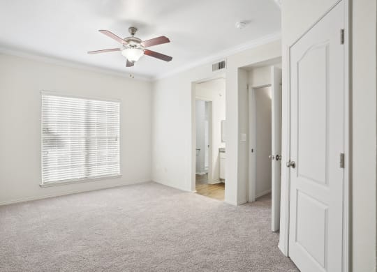 an empty bedroom with a ceiling fan and a door to a bathroom at La Ventura Apartments, Texas