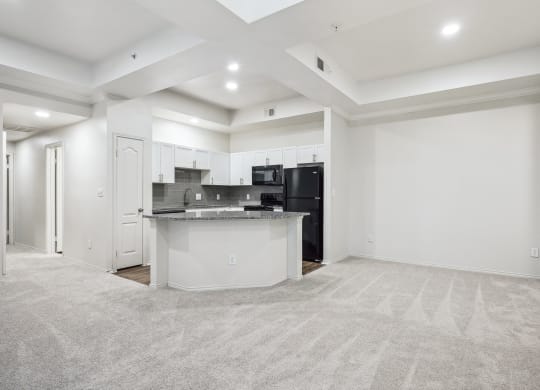 an empty living room with a kitchen with a black refrigerator at La Ventura Apartments, Texas, 75093