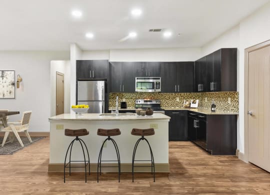 a kitchen with black cabinets and a counter with three stools at Lakeline East Apartments, Cedar Park, TX