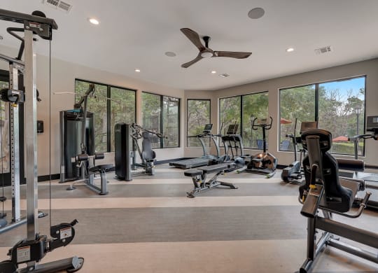 a gym with cardio equipment and windows in a home with a view of the woods