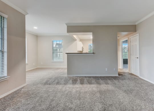 an empty living room with carpet and a kitchen